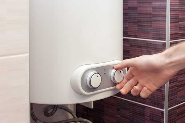 A hand adjusts a knob on an electric boiler.